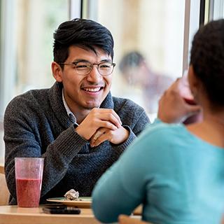 A young male student wearing glasses smiles across a table at a young woman in Market Square, the main TCU dining hall.